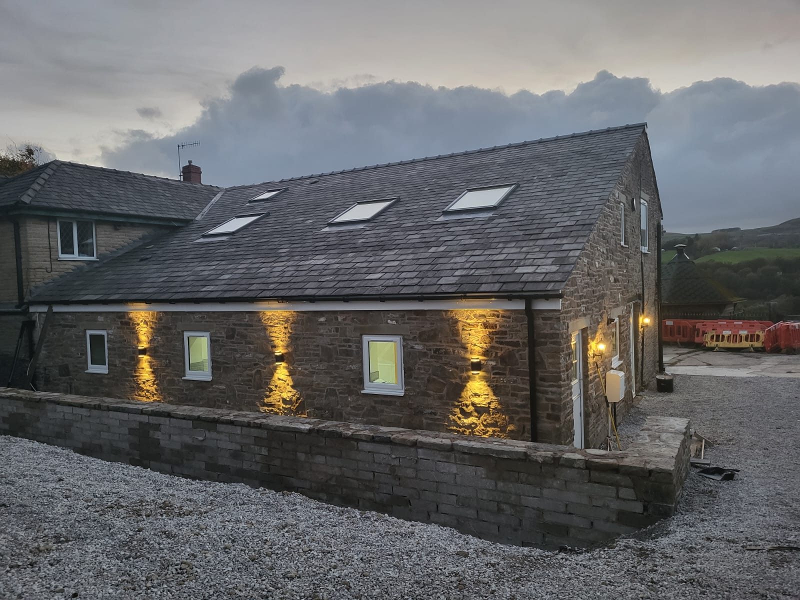 Finished stone barn conversion at dusk with exterior uplighting and slate roof